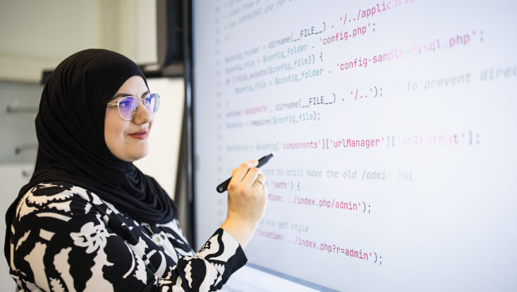Eine Frau mit Kopftuch schreibt an ein Smartboard