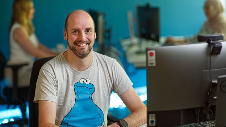 A man wearing a Cookie Monster T-shirt looks at the camera and smiles.